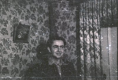 A man appears in a portrait, partially obscured by patterned wallpaper and draped curtains. Visible features suggest a formal...