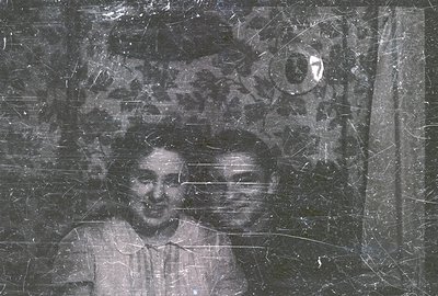 Two men stand closely together in a studio portrait. Visible film grain and extensive scratches indicate age & potential arch...