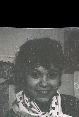 Close-up portrait of a woman smiling, wearing a patterned scarf. Visible film grain and scratches suggest a vintage photograp...