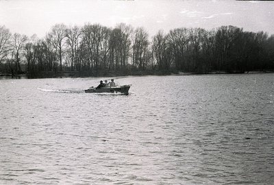 A small motorboat cuts through water, creating a wake. Three figures are onboard, visible as dark silhouettes against the boa...