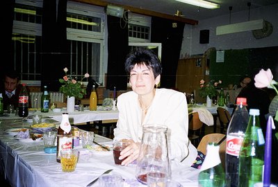 A woman in a cream blazer holds a drink at a table laden with food and drinks. A banquet setting with checkered tablecloths, ...
