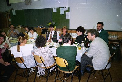 A group gathers for what appears to be a banquet or formal dinner in a gymnasium or community hall. Tables are covered with w...