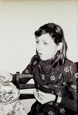 Young woman with dark hair and headband sits at a table, intently examining a small object, possibly jewelry, held in her han...
