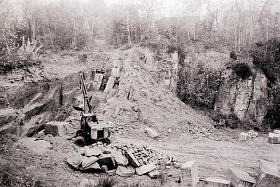 A quarry scene, likely showcasing stone extraction. Machinery and cut blocks are visible against a dramatic, layered rock fac...