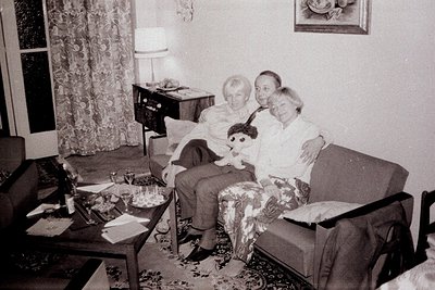 A formal portrait of a family seated on a richly patterned sofa in a parlor. A man in a suit, a woman in a floral dress, and ...