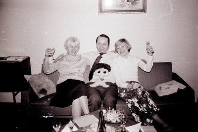 A candid black and white photo depicts three people celebrating on a floral patterned sofa. Two women and one man toast with ...