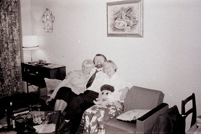 A posed snapshot captures a man and a young boy, seemingly father and son, seated on an armchair amidst mid-century decor. Th...