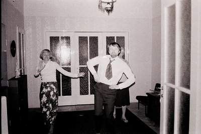 A candid black and white photo shows a man and woman in a hallway, possibly a home interior. The man, with a beard, wears a t...