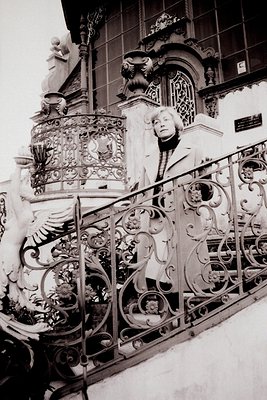 Elegant monochrome portrait shows a woman poised on a grand staircase. Ornate wrought iron railings and a detailed stone balu...