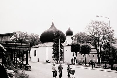 Black & white photo shows a family strolling past a distinctive church with bulbous domes, likely Eastern Orthodox. A roadsid...