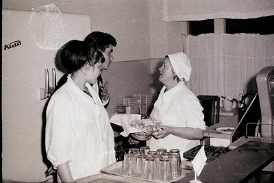Two women in white lab coats and headscarves interact near a large industrial refrigerator ("Холод" branded) in a commercial ...