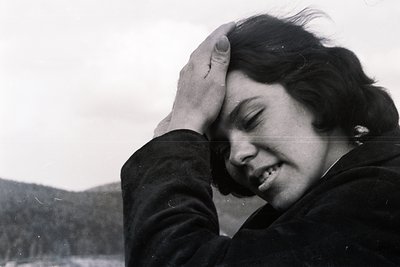 Close-up, black and white portrait. Woman with dark, short hair presses her hand against her forehead, eyes closed, face tilt...