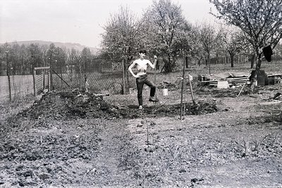 A shirtless young man stands confidently in a newly dug garden plot. He's positioned between a compost heap and a collection ...