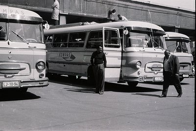 Black and white image showcasing three vintage buses branded with “Kompas” – likely a tour company. Two men in coats stand ne...