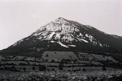 Striking mountain peak dominates the frame, its rocky face marked with snow. Lush, terraced greenery flanks the slope's lower...