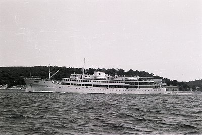 Side view of a passenger ship, likely a coastal ferry, cutting through choppy water. Multi-deck design with visible promenade...