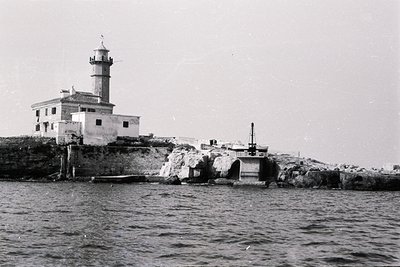 A coastal photograph captures a robust lighthouse built atop rocky cliffs, likely near the sea. The structure features a tall...