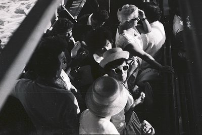 Crowded scene on a ship's deck, showing passengers enjoying the sea breeze. A woman in a straw hat and sunglasses leans over ...