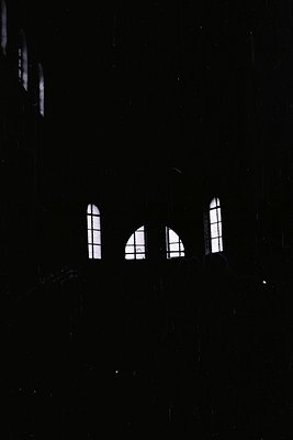 A view through an arched opening reveals architectural details: two tall, narrow windows flank a central, round-arched window...