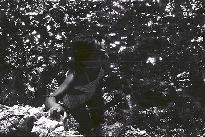 Submerged figure amidst sun-dappled water. A woman, likely in swimwear, appears partially visible near a rocky seabed. The im...