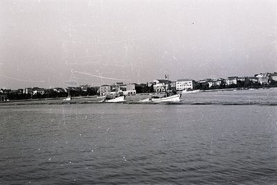 A view of Varna, Bulgaria, featuring several small motorboats traversing the Black Sea. Buildings line the waterfront, some w...