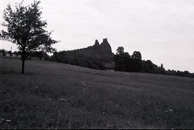 A stark, elevated black and white image captures a dramatic rock formation crowned with ruins, likely a castle or fortress. L...