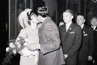 A newly married couple shares a kiss, the bride in a vintage wedding dress and veil, carrying a floral bouquet. Several forma...