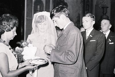 Black & white image captures a wedding ceremony. A young couple stands at an altar; the bride veiled, groom in a military uni...