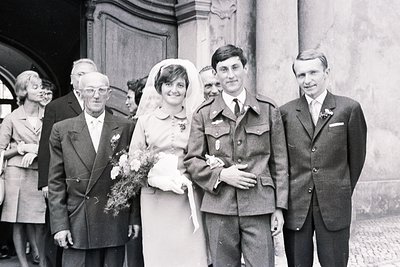Black & white portrait of a wedding party. Bride in a short-sleeved dress & veil, groom in military uniform, alongside older ...