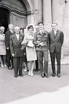 Black and white image showing a newly married couple alongside older relatives and a groomsman. The bride wears a short, A-li...