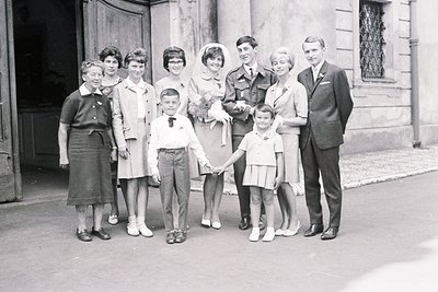 A formal group portrait taken outside a building with architectural details. A woman, presumed grandmother, stands with two y...