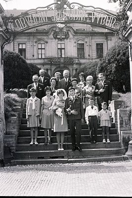 Large formal group portrait, 13 individuals posed on stone steps before an ornate, classical-style building. Architectural de...