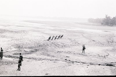 A group of soldiers on horseback traverses a vast, arid landscape with a distant treeline. Several figures stand in the foreg...