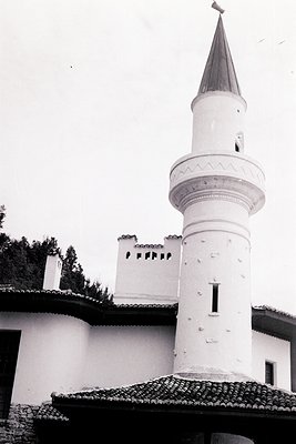 Striking monochrome view of a whitewashed minaret rising above a traditional building. Likely a mosque or religious structure...