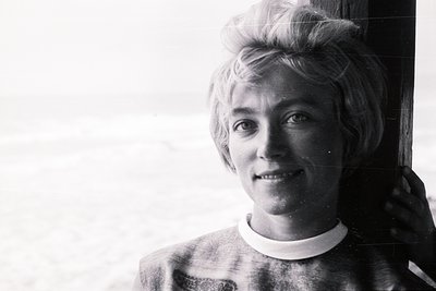A portrait of a young person with a distinctive, styled blonde hairstyle, leaning against a wood-paneled surface. The backgro...