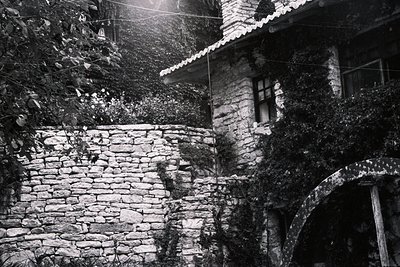 Overgrown stone wall and building facade with arched entryway, possibly a villa or historic structure. Weathered stone constr...