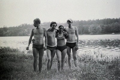 Four young people wade into a lake, wearing vintage swimwear. The scene, likely a vacation or lakeside retreat, features a fo...