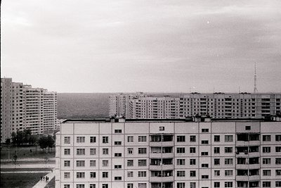 A black and white view showcases a large, Soviet-era apartment complex with repetitive balconies and windows, extending into ...