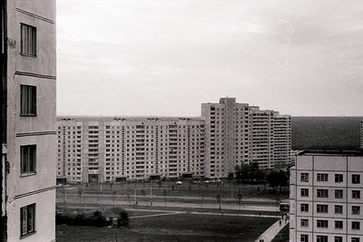 Elevated view of stark, brutalist apartment blocks and a central tower. Likely post-war Soviet era architecture. Identical wi...