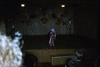 Vintage stage performance featuring a performer in a striking red-and-white striped suit with a white mask, likely from the 1...