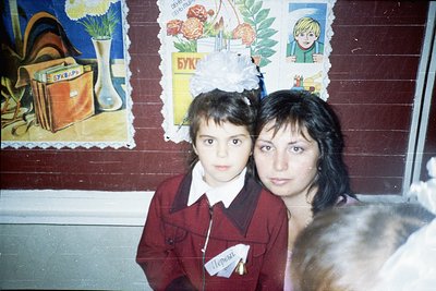 Two women in matching red school uniforms pose indoors, likely in a Soviet-era or Eastern Bloc school. The girl wears a name ...