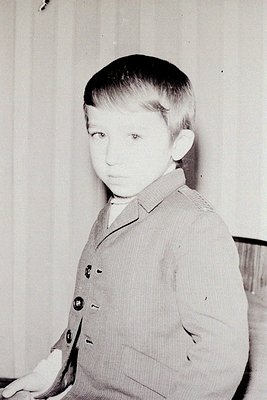 Young boy in a mid-century formal vest, likely 1950s–1960s. Plain backdrop suggests studio portrait. Classic hairstyle and at...