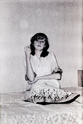 Vintage portrait of a woman seated on floral-patterned upholstery, mid-20th century. She wears a lace-collared blouse, round ...