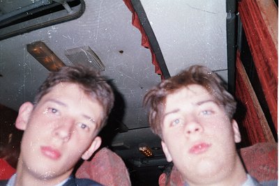 Vintage selfie-style photo of two young men in a dimly lit, possibly indoor party setting. Blurred faces suggest candid, unpo...