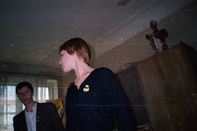 Vintage indoor portrait featuring two individuals in a dimly lit, possibly abandoned or aged room. The person in focus wears ...