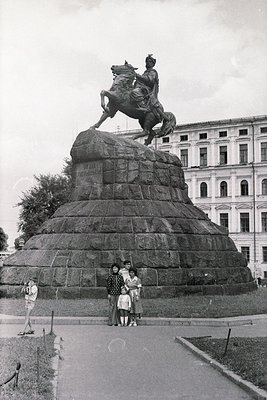 Equestrian statue atop a rugged stone pedestal, likely honoring a historical figure, set against neoclassical-style buildings...