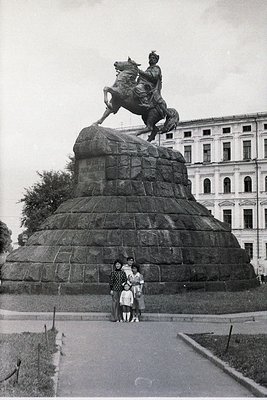 Equestrian statue atop a stepped stone pedestal, likely honoring a historical figure, with three people posing in front. The ...