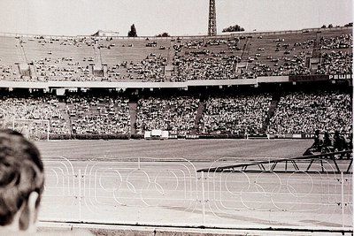 Black-and-white shot of a packed stadium, likely from the 1960s–1970s, featuring tiered seating filled with spectators. The f...