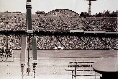 Vintage black-and-white stadium shot showcasing Soviet-era architecture with Cyrillic signage ("Жизнь" = "Life"). Crowded sta...