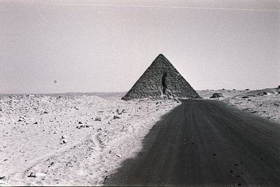 Black-and-white shot of the Great Pyramid of Giza, viewed from the Sphinx’s direction along the Valley Temple road. The pyram...